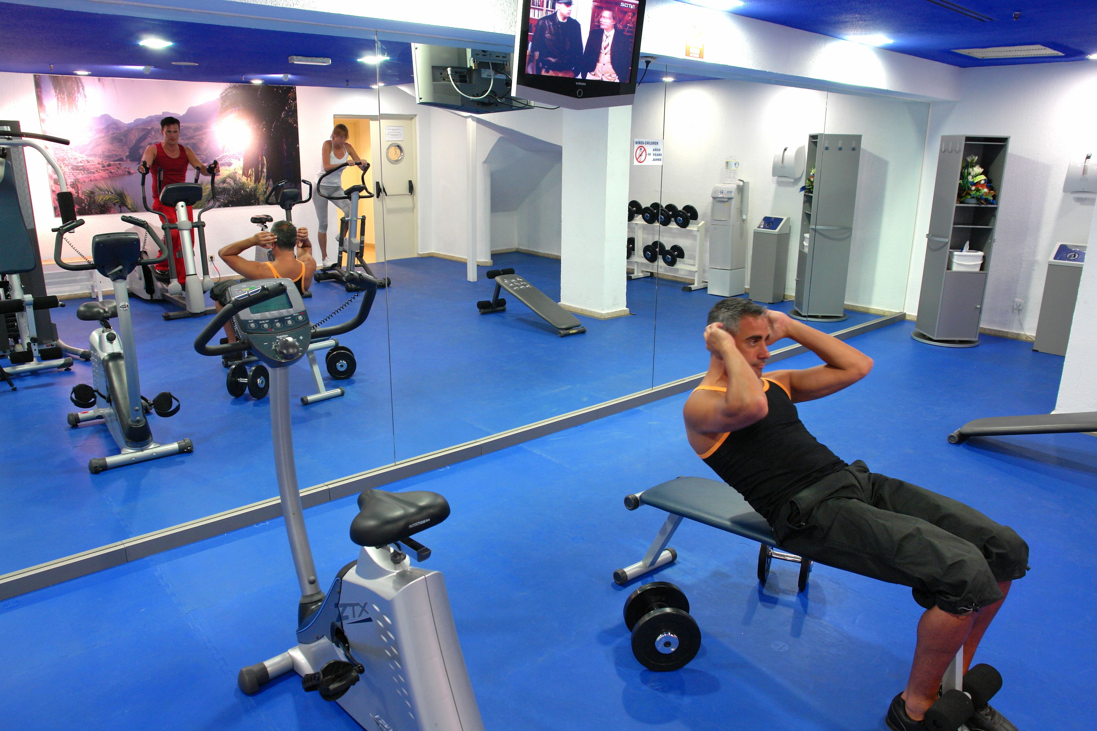Une salle de sport équipée de matériel d’exercice, d’un téléviseur et dotée d’un sol bleu.