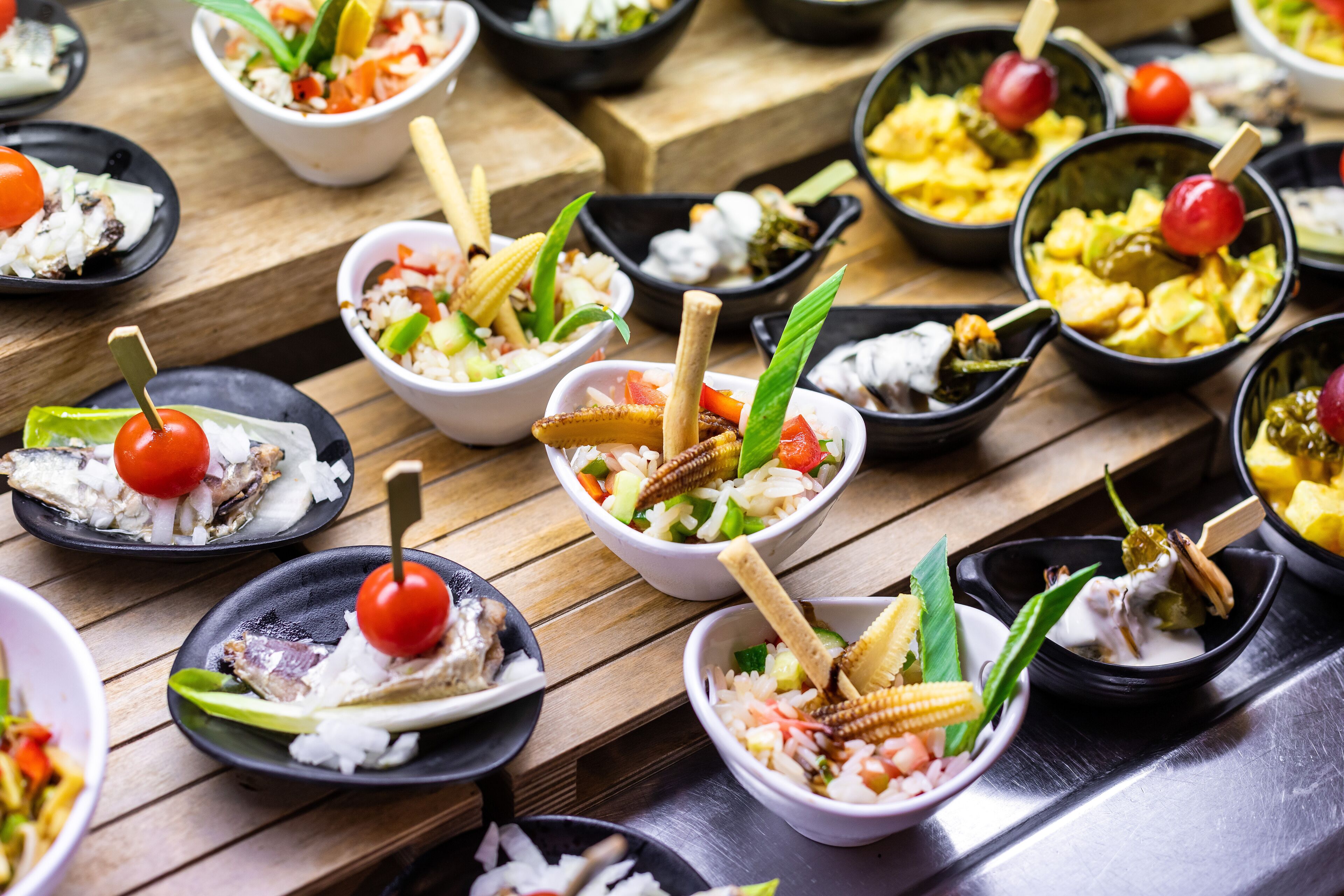 A variety of small bowls containing different dishes, arranged on a wooden table.
