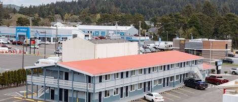 A motel with a red roof, multiple parking spaces, and a view of a forested hill in the background.