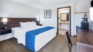 A hotel room with a bed, bedside table, lamp, and a small desk with a chair.