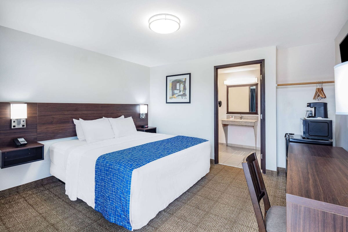 Une chambre d’hôtel comprenant un lit, une table de chevet, une lampe et un petit bureau avec une chaise.
