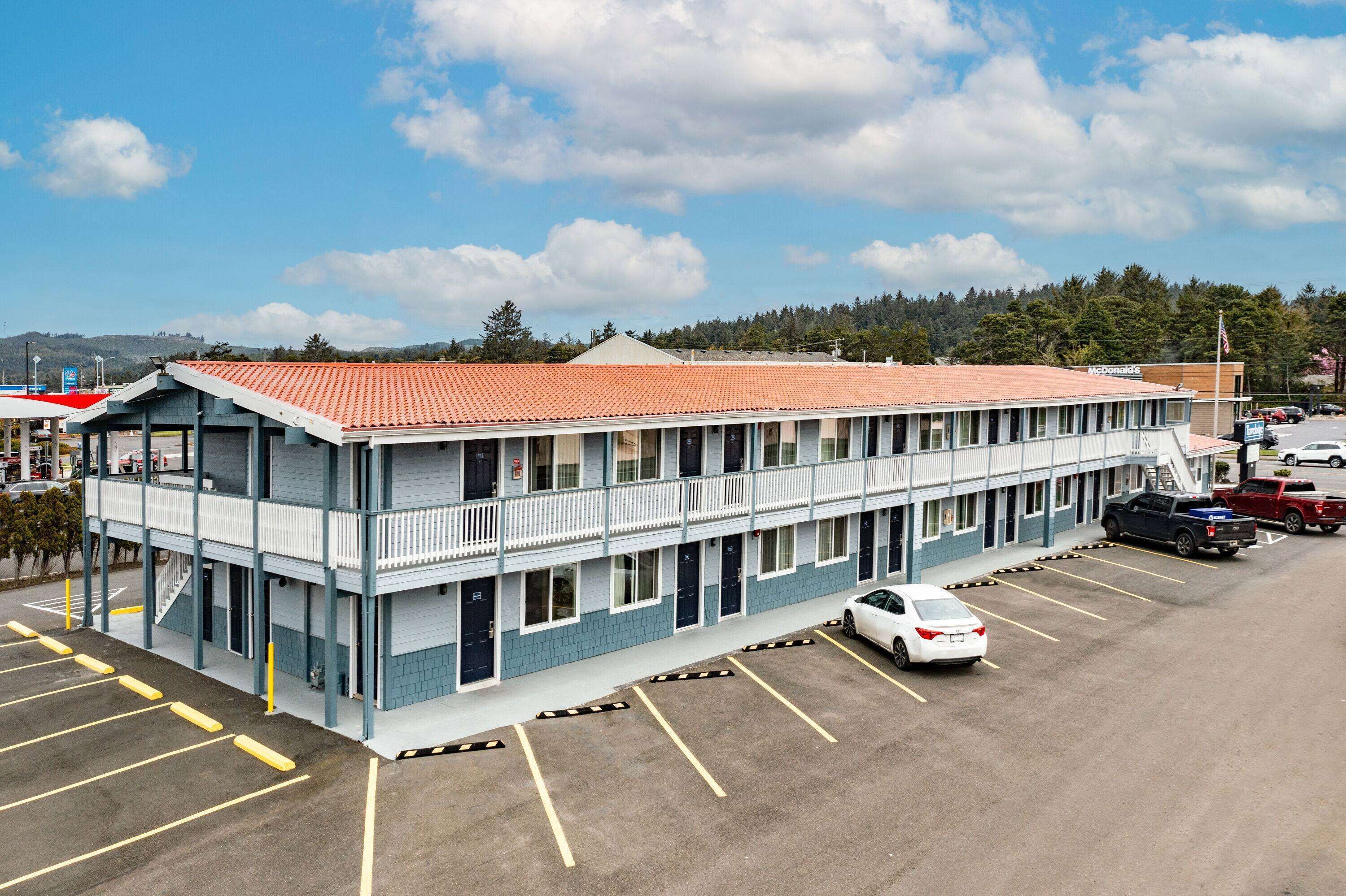 A motel with a red-tiled roof, a balcony on the second floor, and a parking lot with several cars.