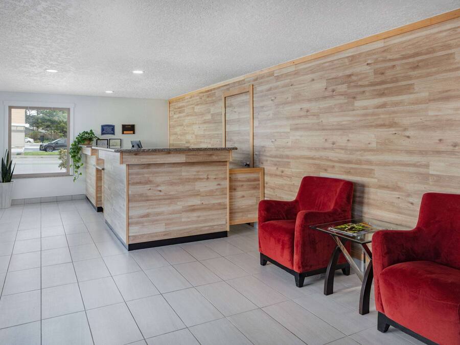 Un área de recepción con un mostrador de madera, dos sillas rojas y una mesita con una revista.
