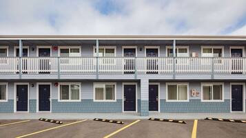 A multi-story motel with a balcony on the second floor, individual rooms with doors, and a parking area with marked spaces.