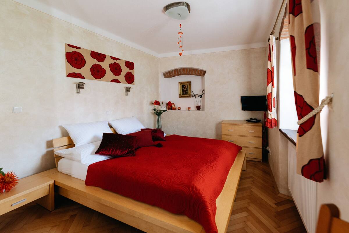Ein Schlafzimmer mit einem hölzernen Bett, einer roten Decke, einem Nachttisch, einer Kommode und einem Spiegel.
