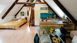 Een kleine slaapkamer onder de dakpannen, met een bed, een klein tafeltje met een vaas zonnebloemen en een glazen eettafel.