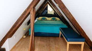 A loft bedroom with a sloped ceiling, a bed with a green bedspread, a blue bench, and wooden beams.