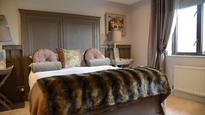 A bedroom with a large bed, a fur throw, and a painting on the wall.
