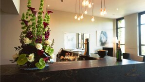 A modern kitchen with a dark countertop, hanging pendant lights, and a vase of flowers on the counter.