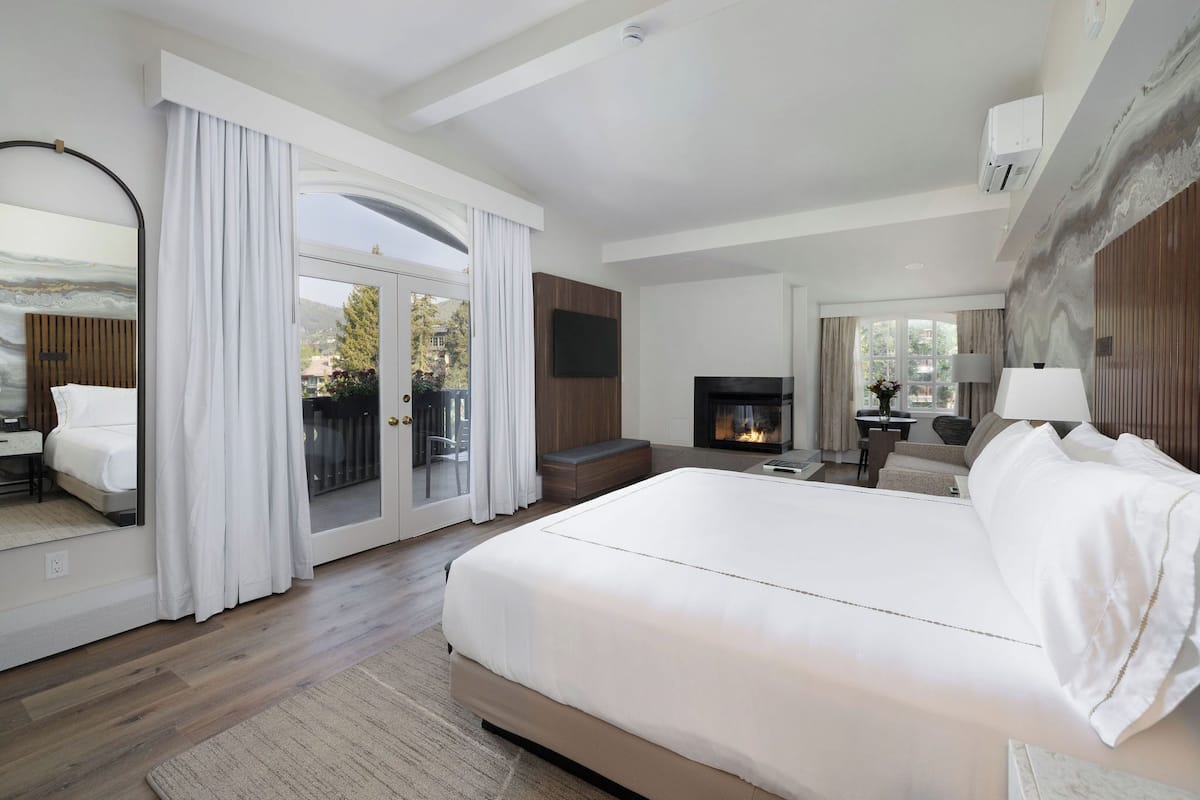 A modern hotel room with a large bed, a fireplace, a television, and a balcony with curtains.