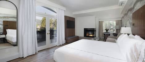 A modern hotel room with a large bed, a fireplace, a television, and a balcony with curtains.