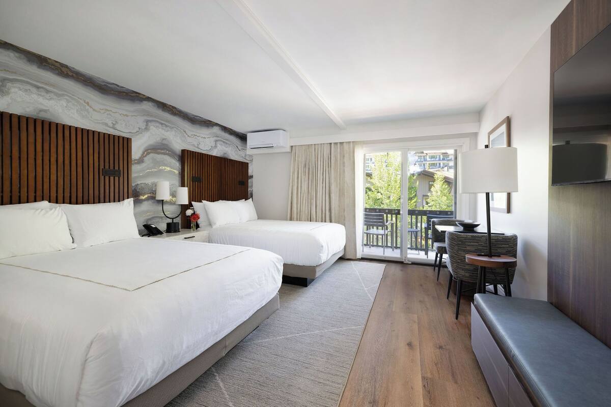 A hotel room with two beds, a sofa, a small table, and a balcony with a view.