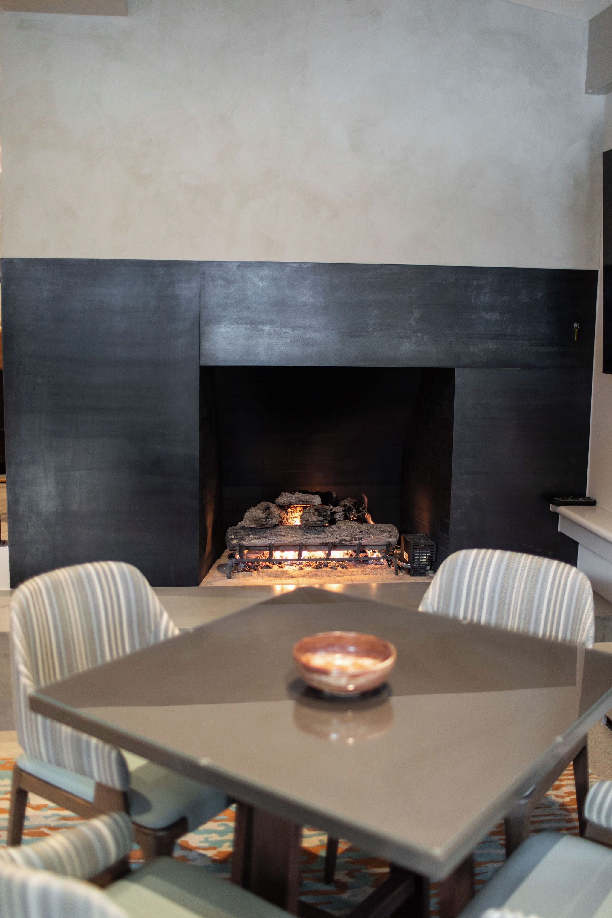 A modern living room with a fireplace, a dining table, and striped chairs.
