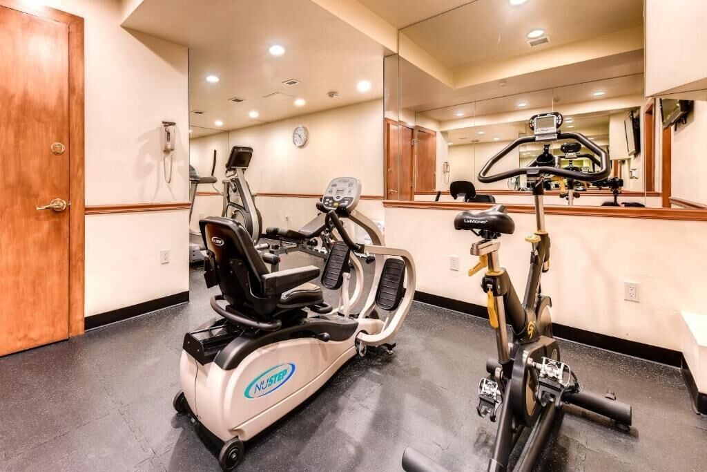 Un gimnasio con bicicletas estáticas, una cinta de correr y un espejo grande.