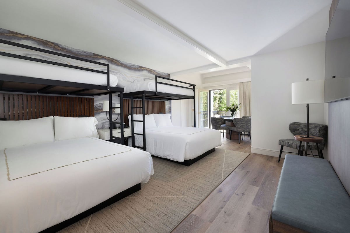 A hotel room with two beds, a bench, a desk, and a chair.