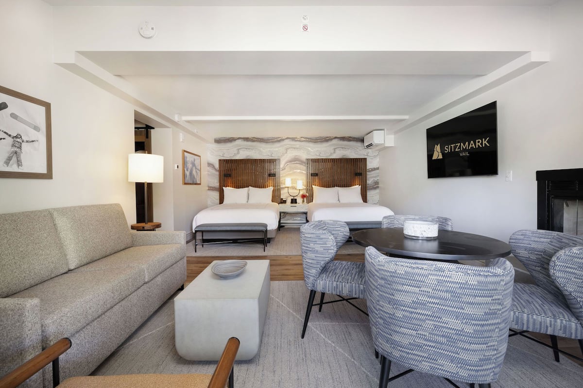 A hotel room with a sofa, two beds, a dining table, and chairs.