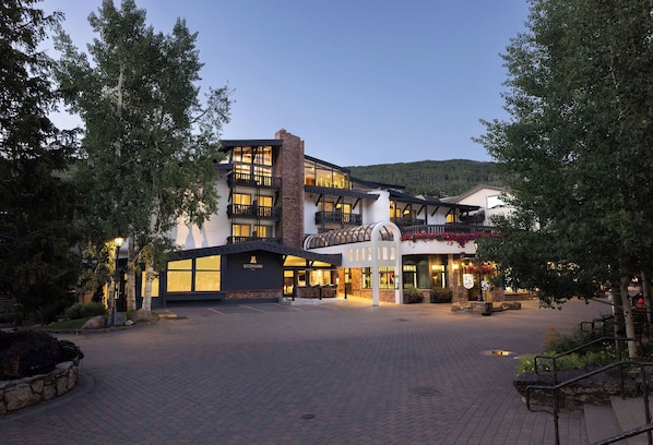 Welcome to a serene oasis surrounded by lush greenery and trees, with a modern entrance and large windows.
