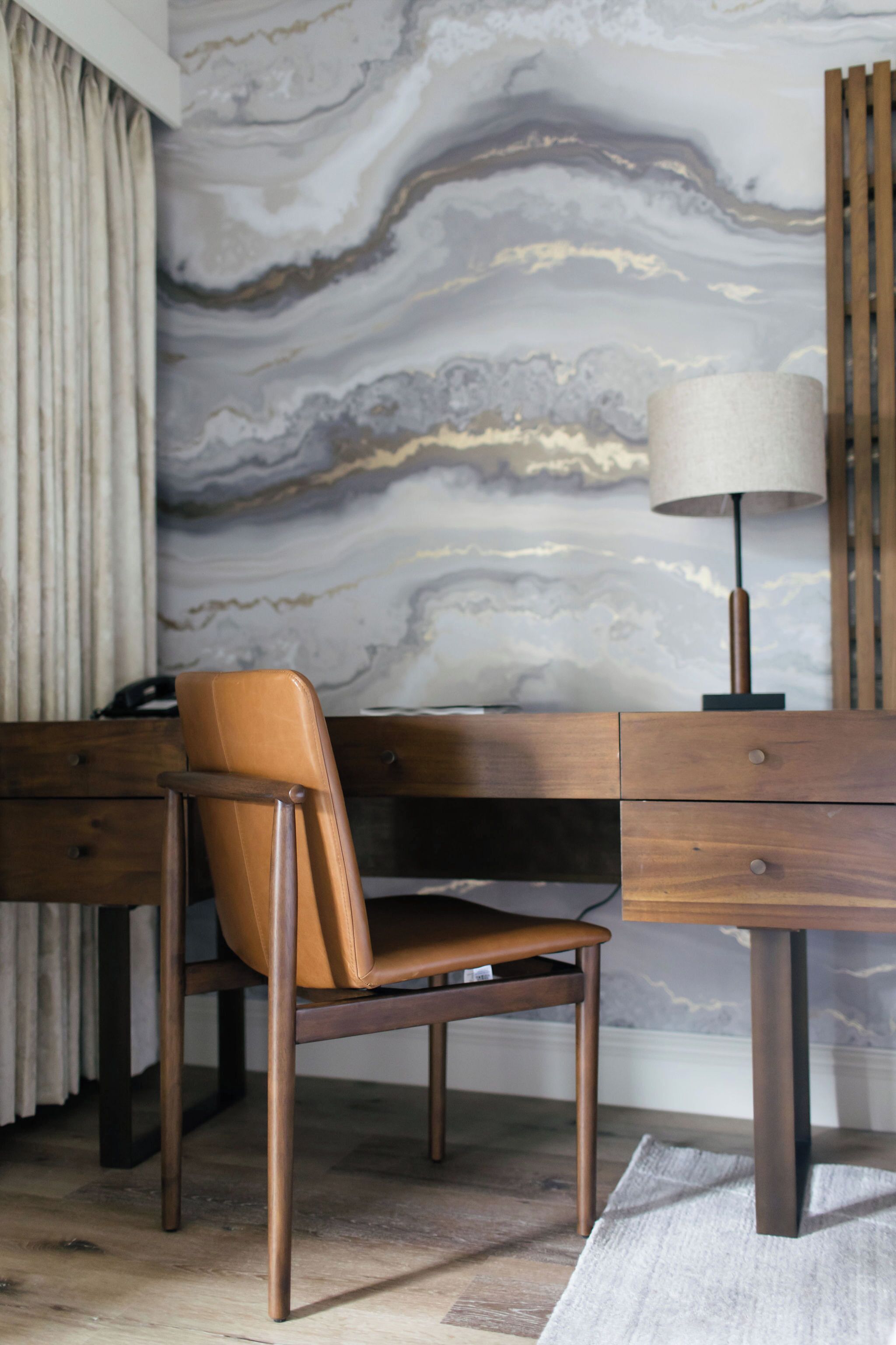 A modern room with a marble wall, a wooden desk, a leather chair, and a lamp.