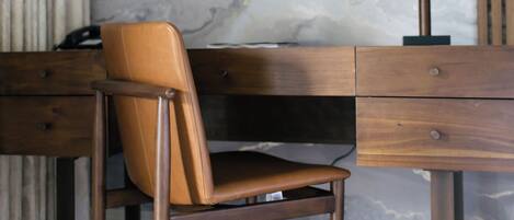 A modern room with a marble wall, a wooden desk, a leather chair, and a lamp.