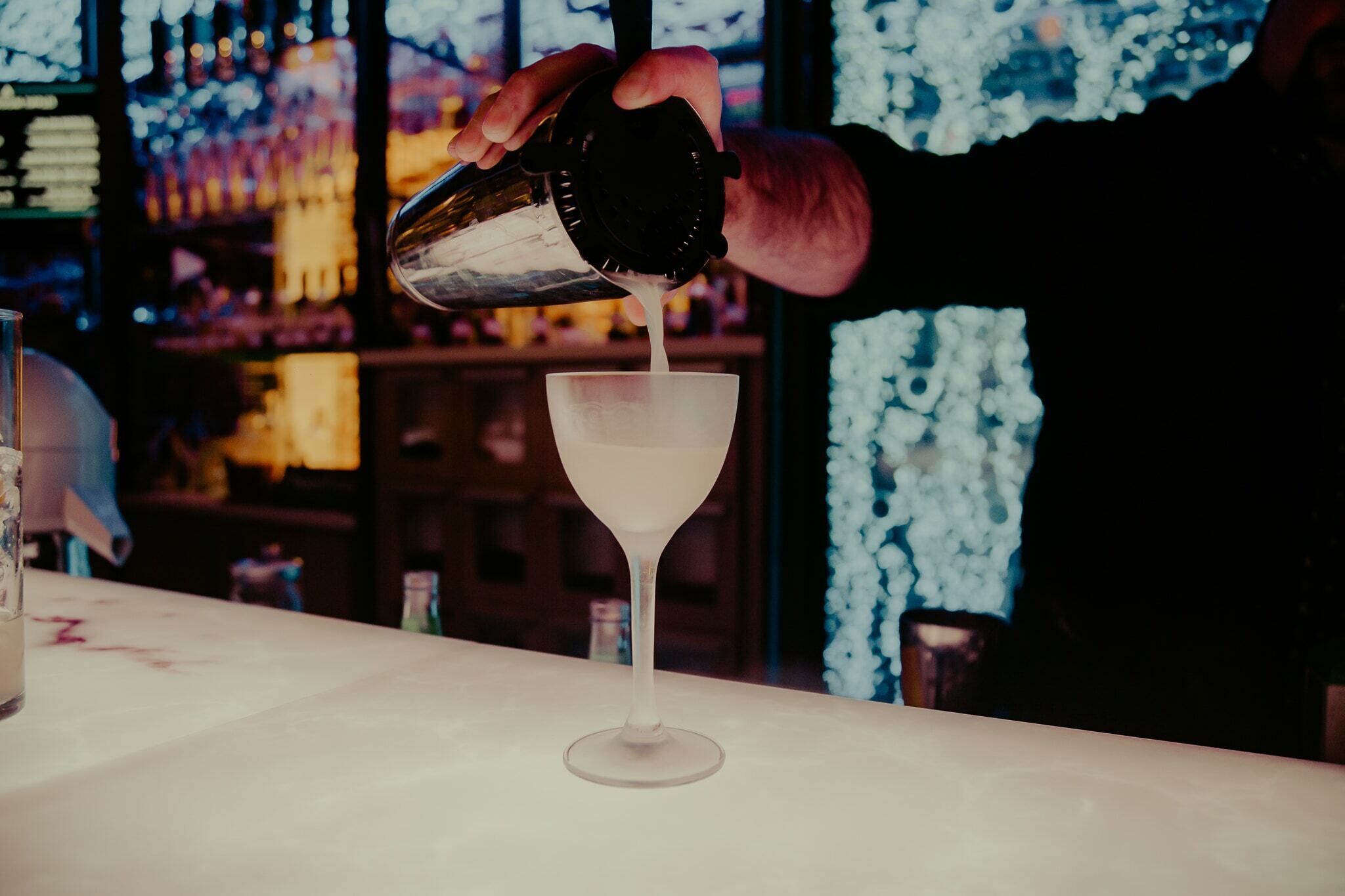 A person pouring a liquid into a martini glass.