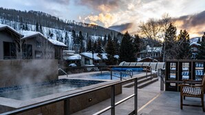 A spa area with a hot tub, outdoor seating, and a view of snow-covered houses and mountains. - Sitzmark Vail (Vail)