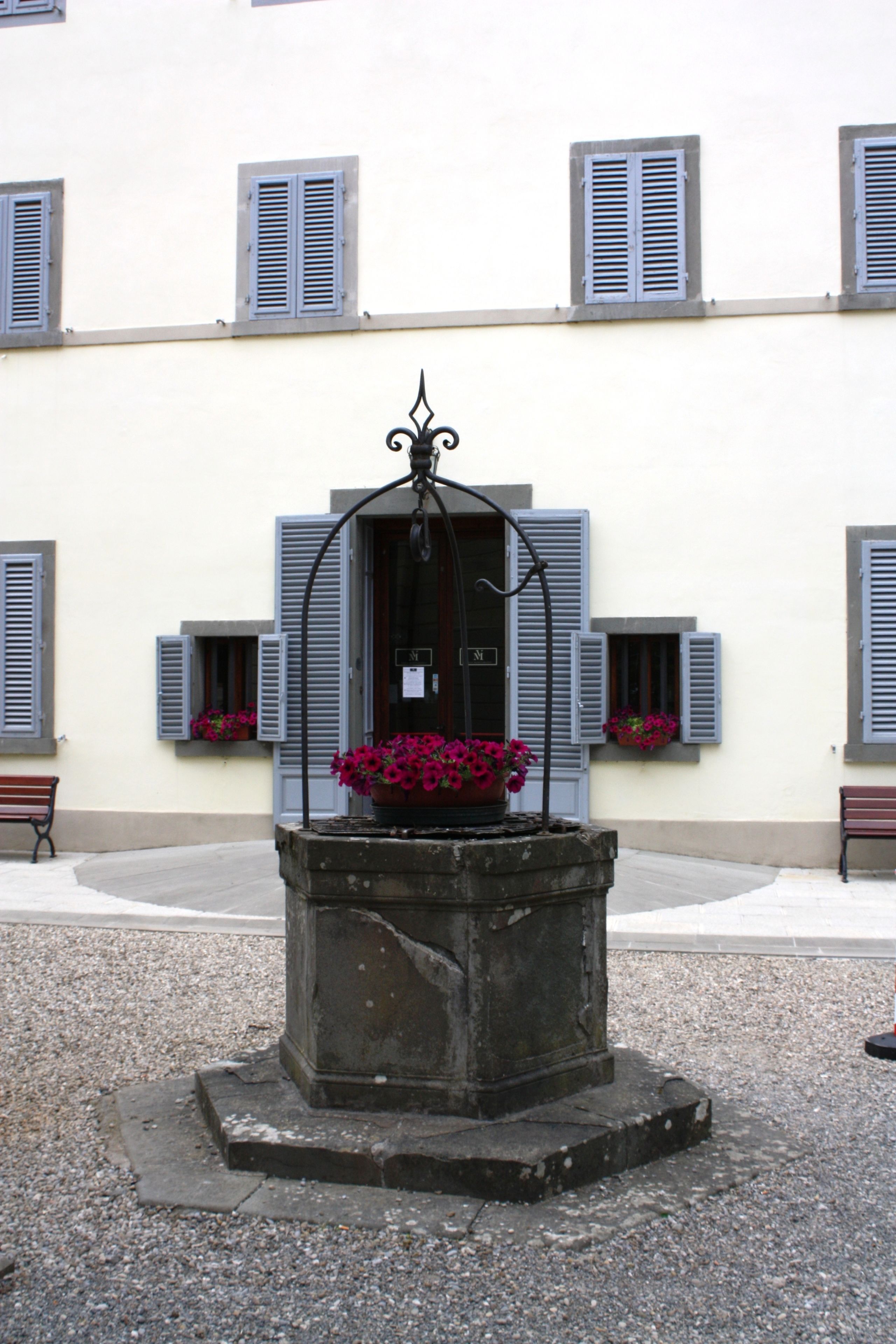 Ein Brunnen mit Blumen vor einem Gebäude mit zahlreichen Fenstern und Fensterläden.