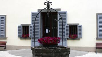Ein Brunnen mit Blumen vor einem Gebäude mit zahlreichen Fenstern und Fensterläden.