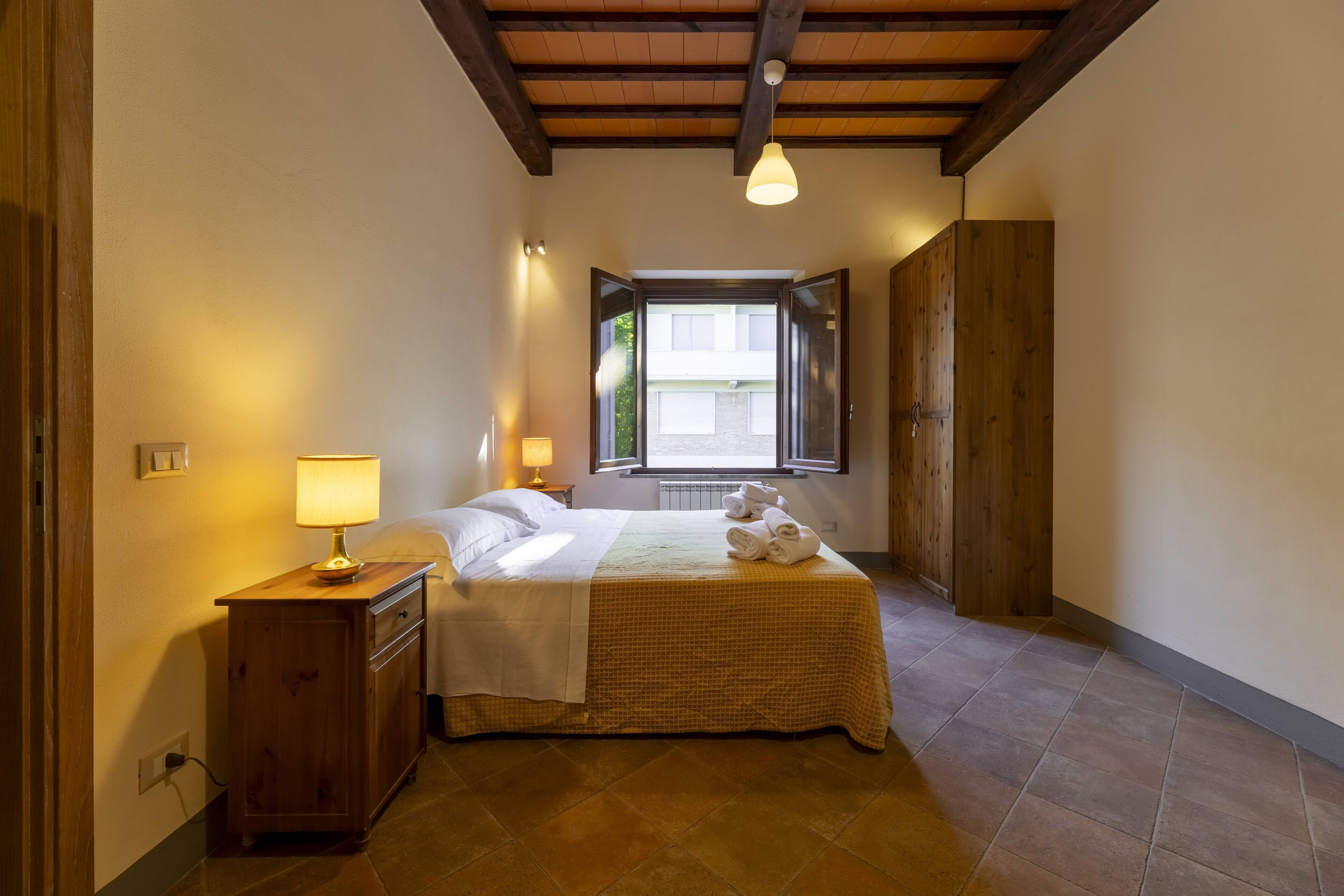 Ein Schlafzimmer mit einem Bett, einem Nachttisch, einer Lampe, einem Fenster und einem Holzschrank.