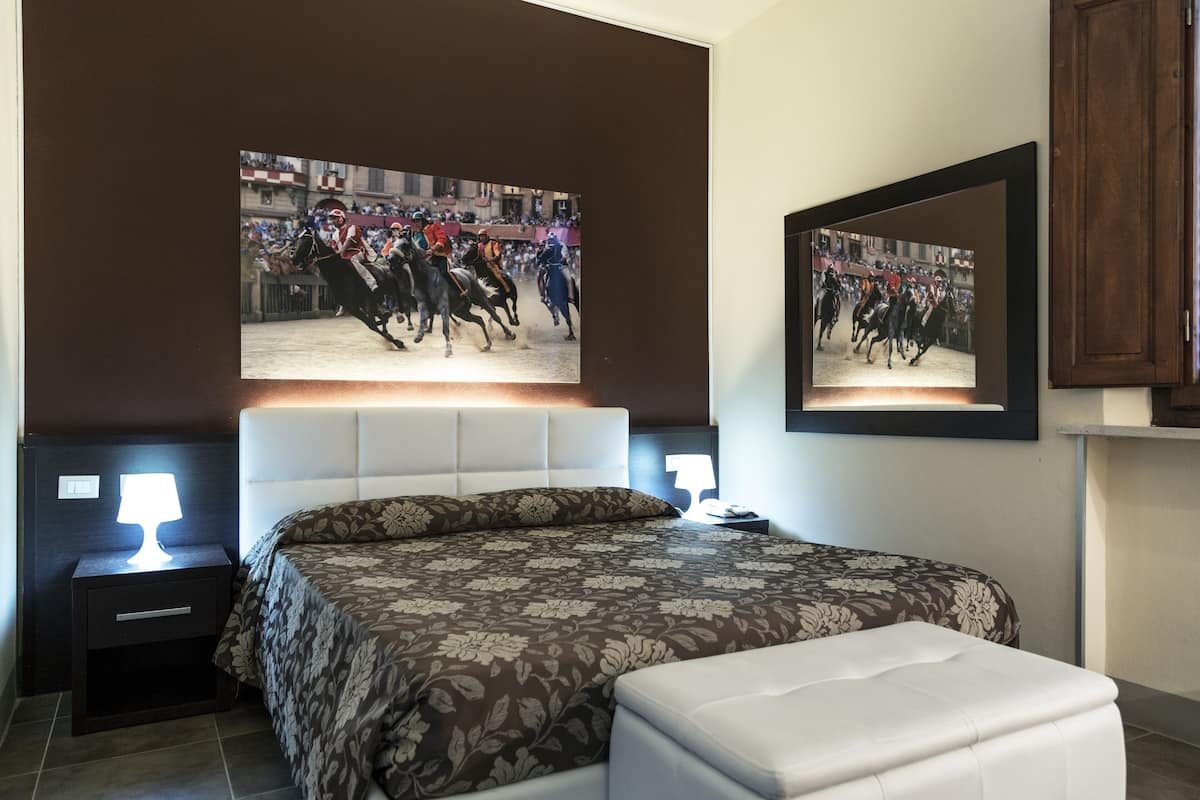 A bedroom with a large bed, two bedside tables with lamps, a nightstand, and a wall-mounted mirror.