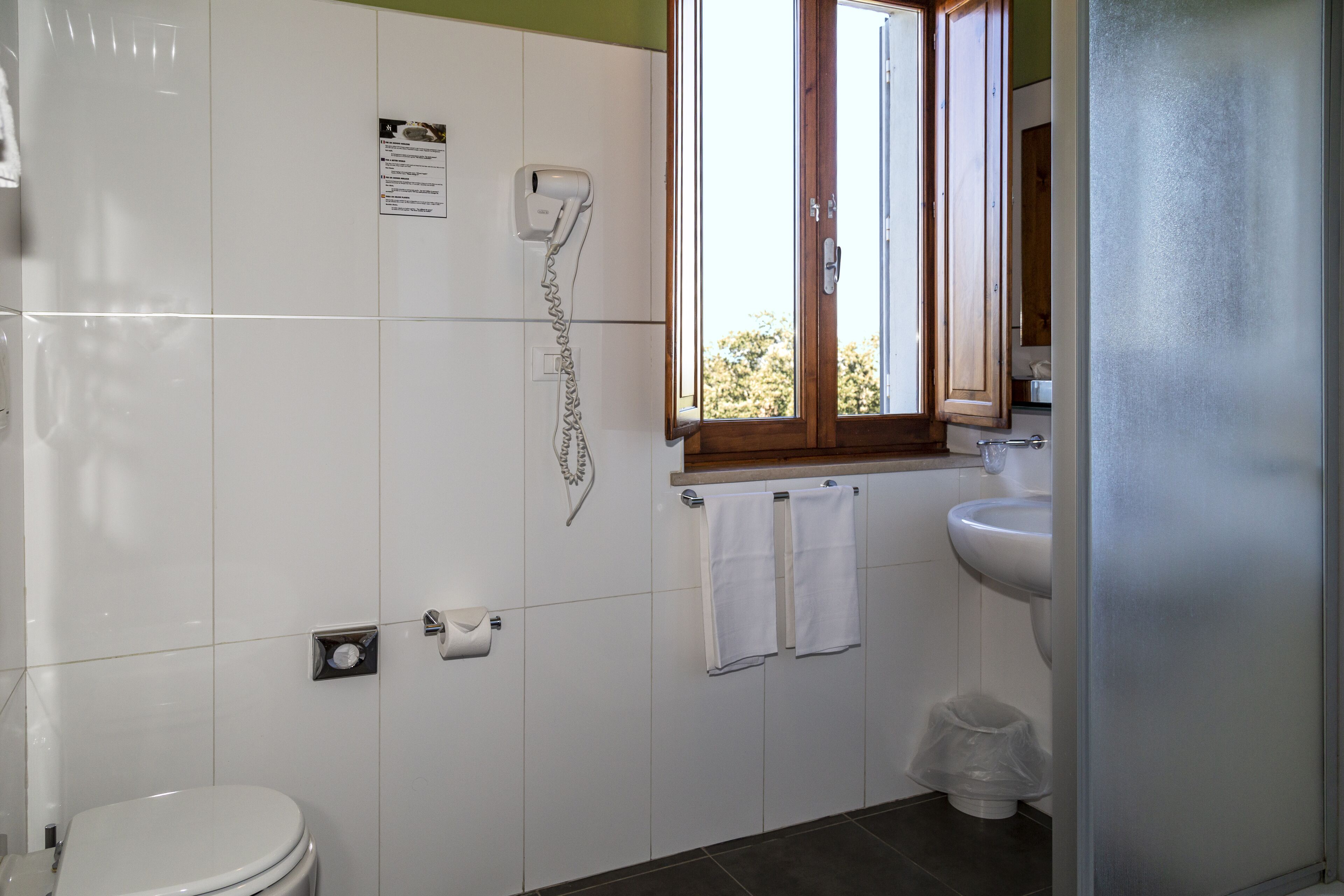 Een badkamer met toilet, wastafel, handdoekrek en een raam.