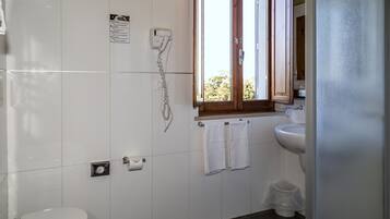 Een badkamer met toilet, wastafel, handdoekrek en een raam.