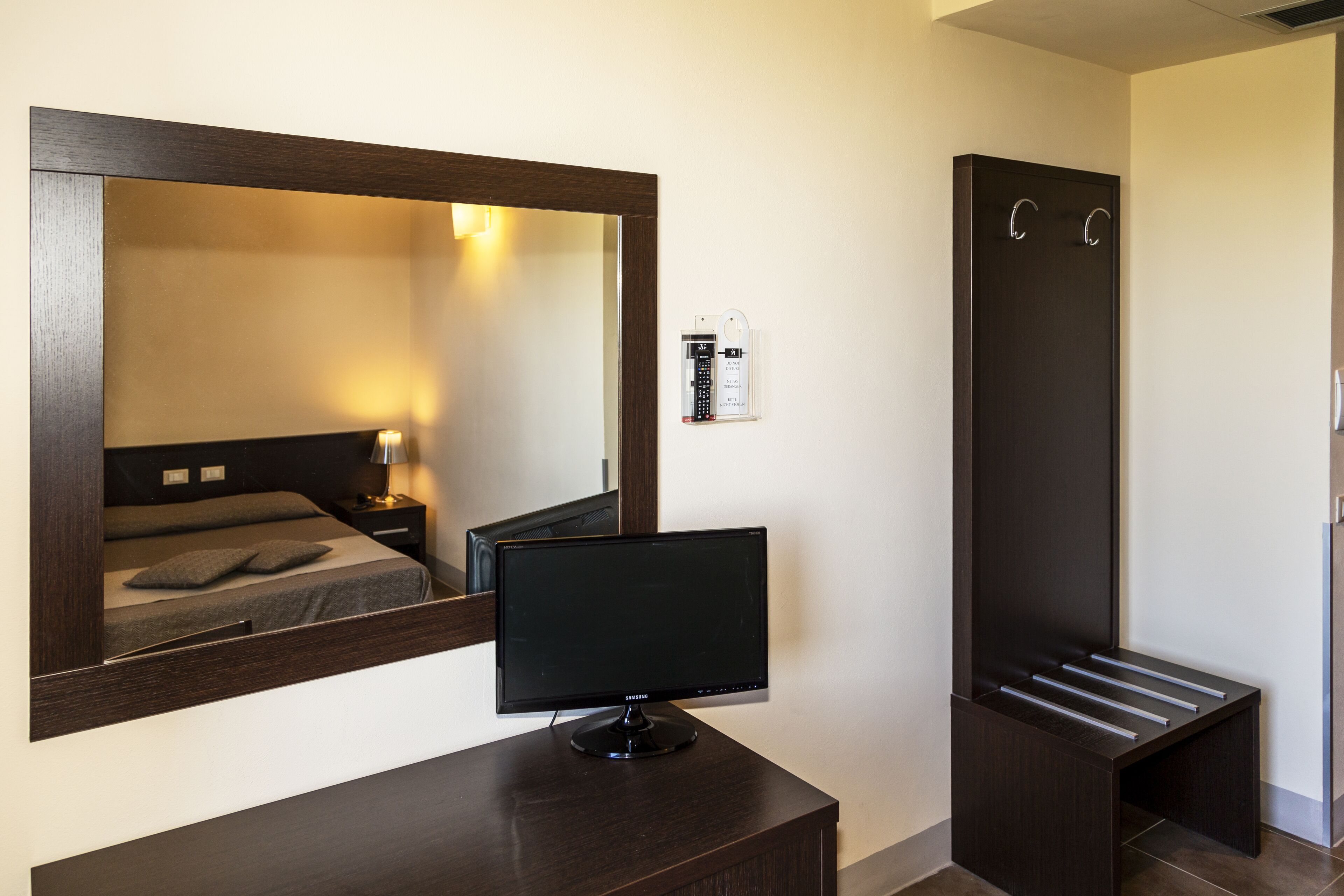 Una habitación de hotel con cama, mesita de noche, televisor, armario y espejo.