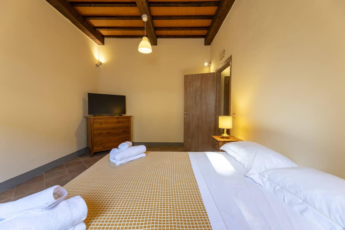 A bedroom with a bed, a wooden dresser, a television, and a door.
