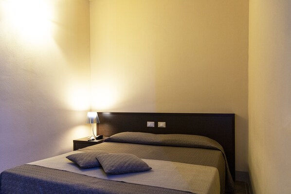 Una habitación de hotel con una cama, una mesita de noche y una lámpara.