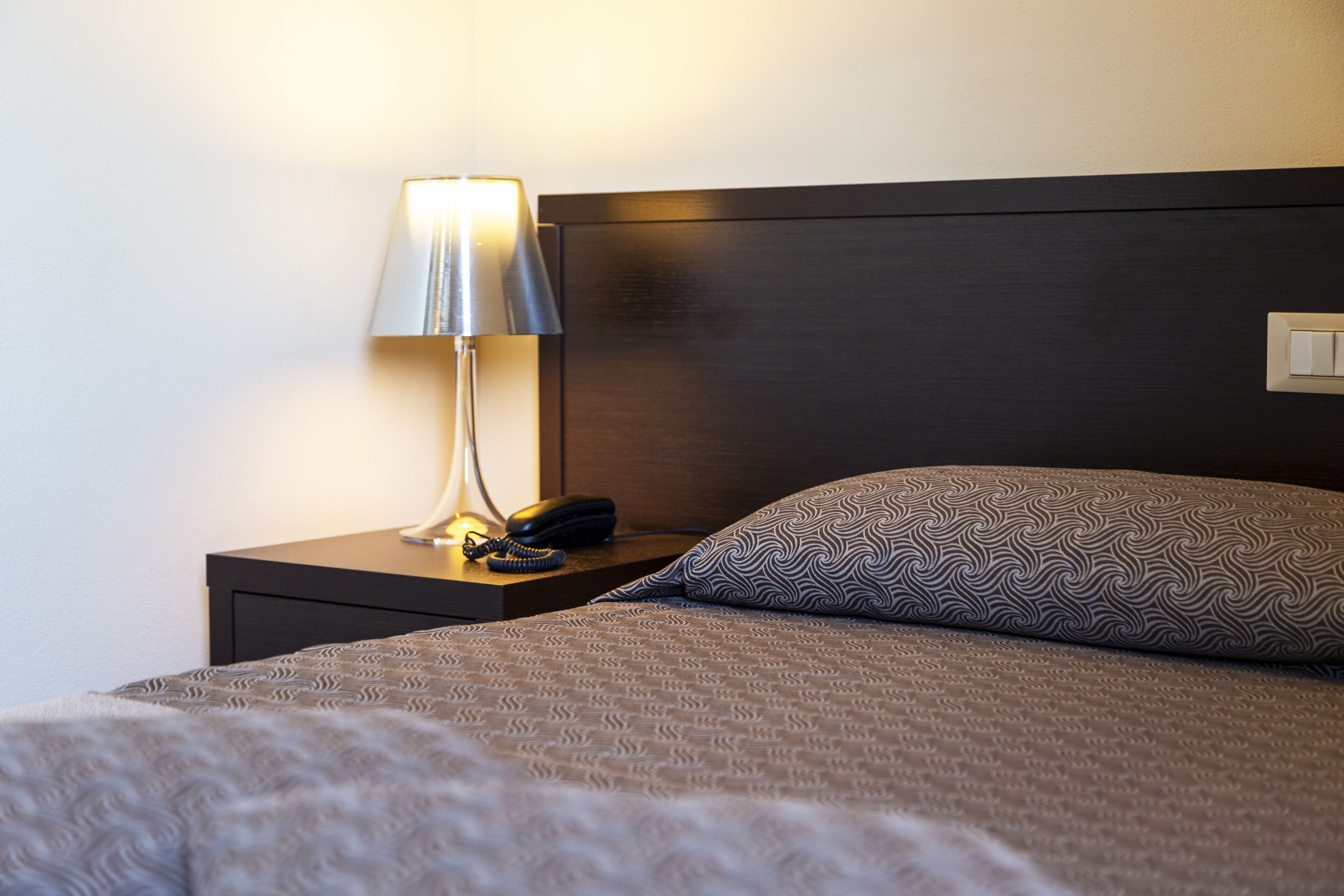 Una cama bien tendida con una almohada estampada y una lámpara de noche en una mesita de madera oscura.