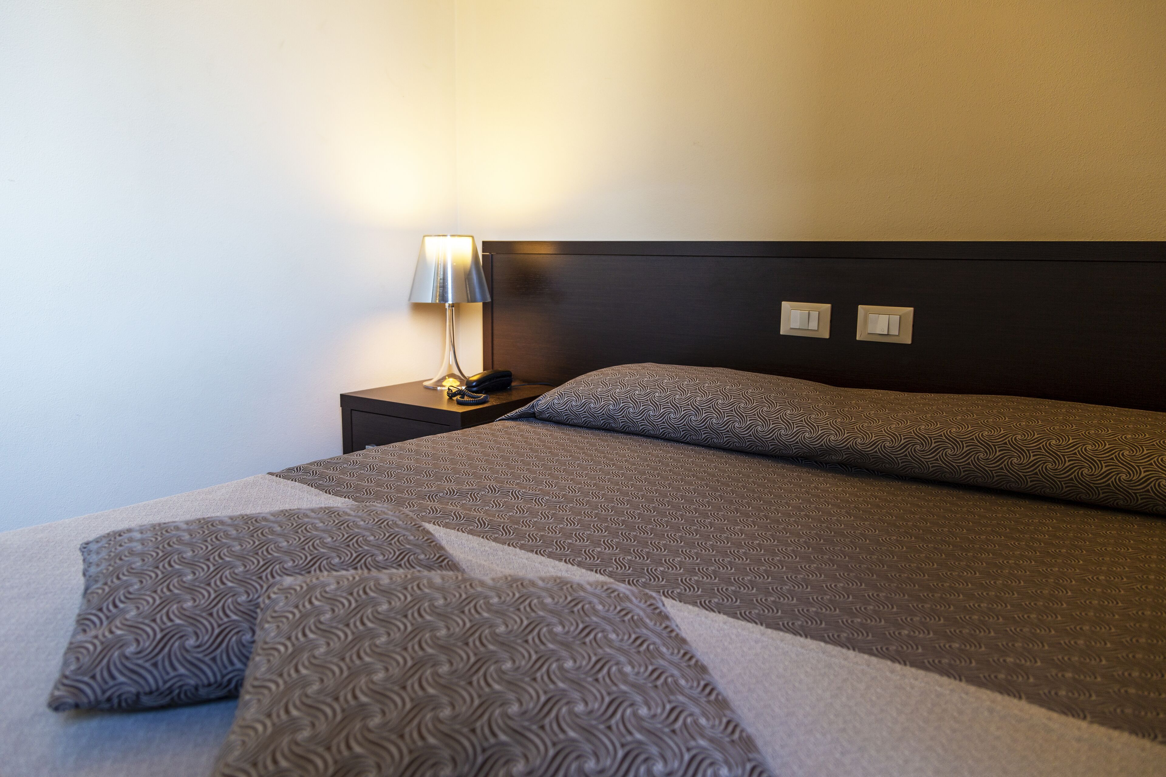 Een opgemaakt bed met gestreepte kussens en een bedlampje.