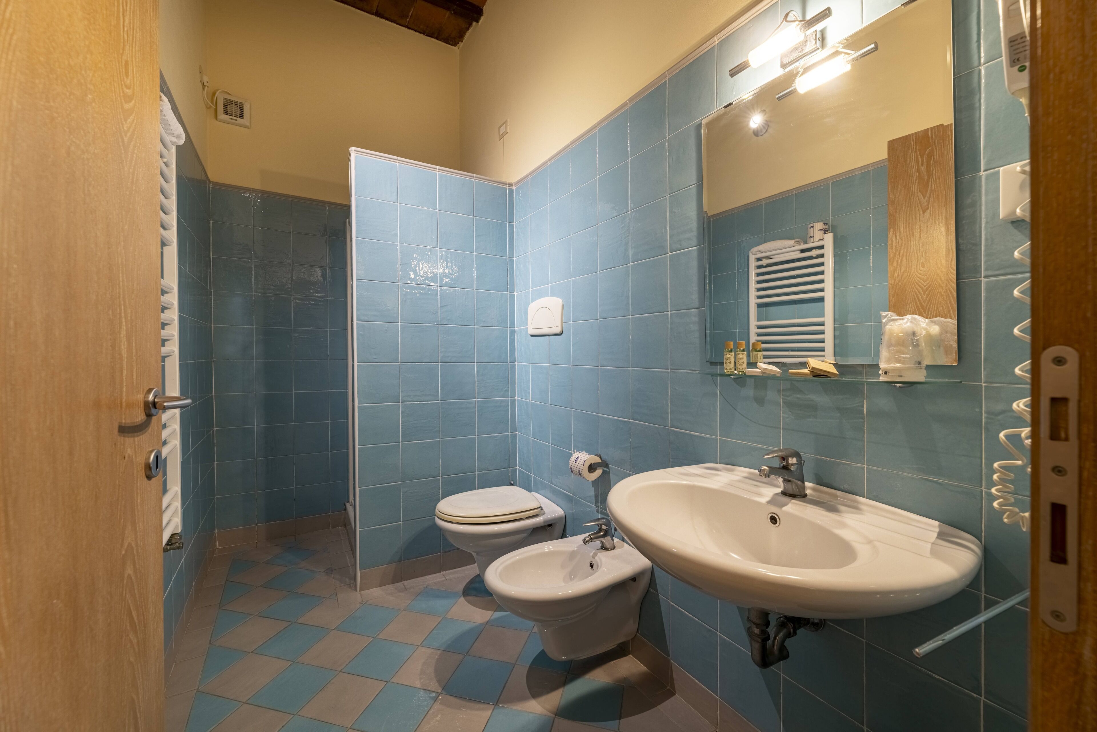 A bathroom with blue tiles, a toilet, a bidet, and a sink.