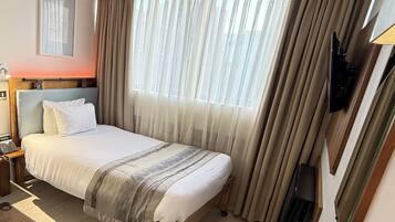 A hotel room with a bed, curtains, a TV, and a bedside table.