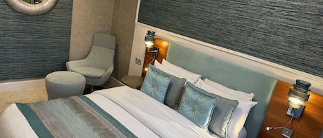 A hotel room with a bed, a chair, a round mirror, and wall-mounted lights.