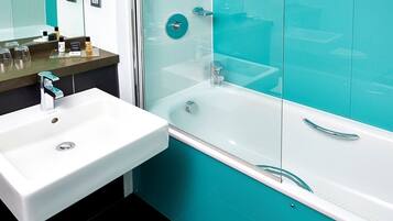 Un baño moderno con un lavamanos blanco, ducha con cerramiento de vidrio y azulejos verde azulado.