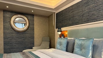 Una habitación de hotel moderna con una cama grande, un espejo redondo, una silla y un cabecero con varias almohadas.