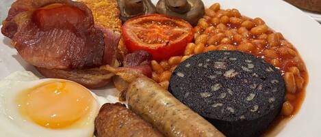 A breakfast plate with bacon, eggs, sausages, mushrooms, baked beans, and toast.
