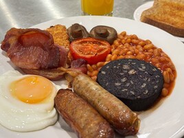 A breakfast plate with bacon, eggs, sausages, mushrooms, baked beans, and toast.