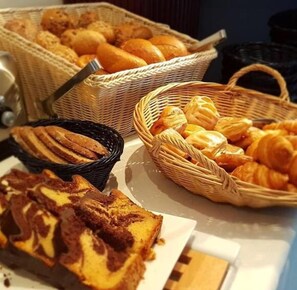 Una mesa de bufé con diversos productos de panadería, incluyendo pan, pasteles y un pastel.