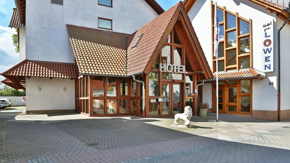 Un hotel de estilo arquitectónico europeo tradicional, que destaca por una entrada imponente con grandes ventanales y un techo de tejas.