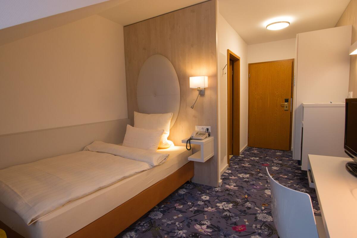 Een hotelkamer met een bed, nachtkastje, lamp en een televisie.