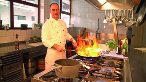 Een kok in een keuken met een grote kookplaat, pannen en een raam.
