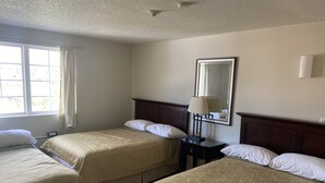 A hotel room with two beds, a nightstand with a lamp, a large mirror, and a window with curtains. - Caravan Inn Motel (Niagara Falls)