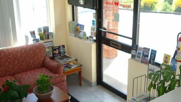 A room with a sofa, a coffee table with a plant, a small table with magazines, and a door leading outside. - Caravan Inn Motel (Niagara Falls)