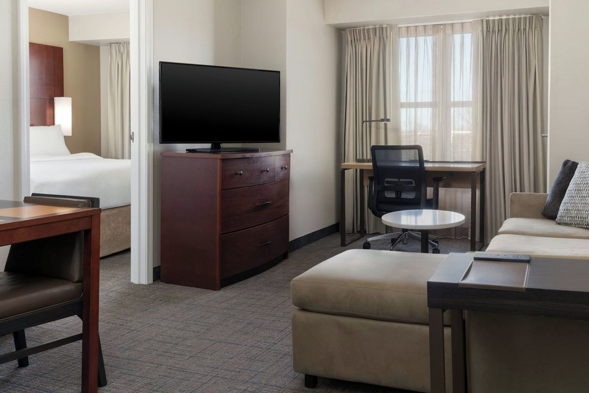 A hotel room with a bed, a TV on a wooden cabinet, a desk with a chair, and a sofa.